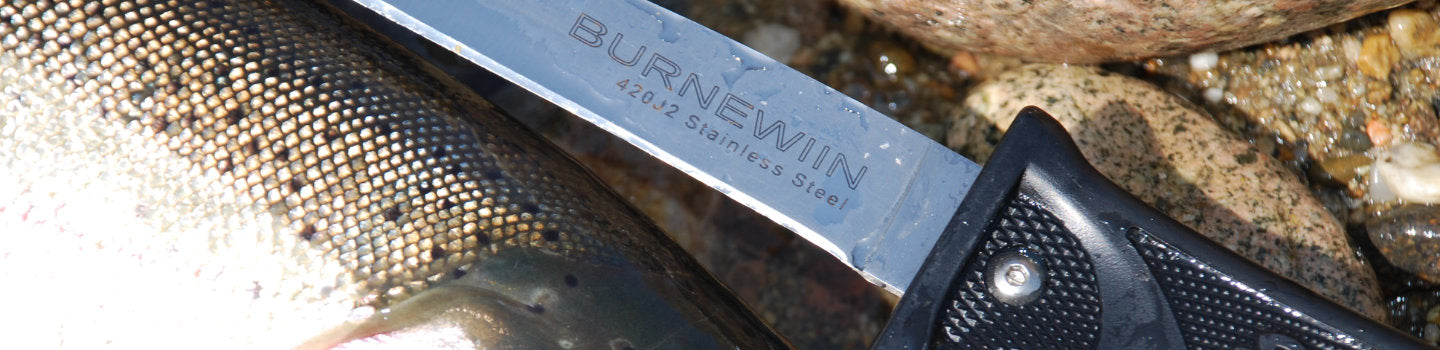 A close-up view of the Burnewiin KN3610 Fillet Knife and a fish, both on some rocks and waiting for meal preparation.