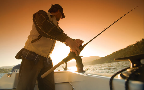 A fisherman is adjusting his Burnewiin RH5710 Rod Holder that is mounted on the gunwale, with the sun setting in the background.