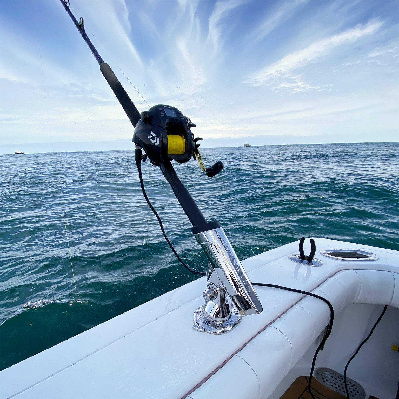 A fishing rod with a line in the water, cradled in the Burnewiin RH8420 Stainless Steel Rod Holder and GM650 mounted on the stern gunwale.