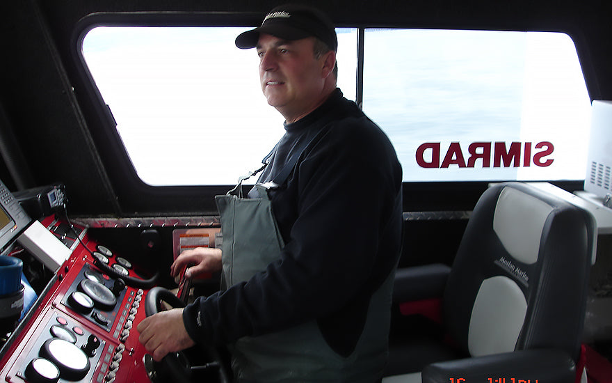 Mark Oldenstadt, a satisfied Burnewiin dealer, stands in the pilot house and at the controls of his fishing boat.